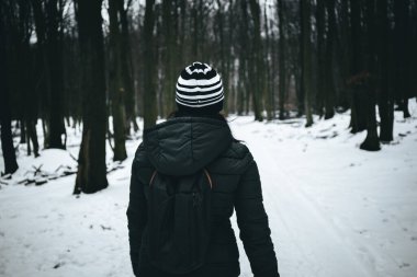 Siyah ceketli genç kız karda yürüyor. Ormanda kış