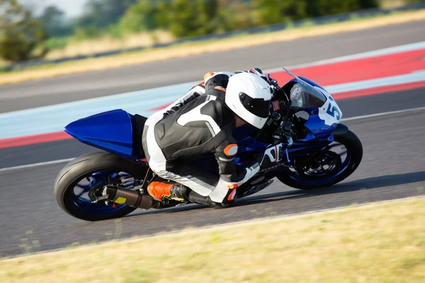 Side view of a motorcycle rider riding on a blue sportbike through a corner at high speed.