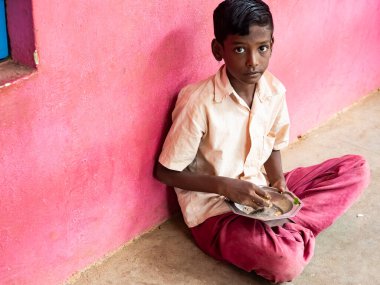 PUDUCHERRY, TAMIL NADU, Hindistan - Aralık 2018. Tanımlanamayan yoksul sınıf arkadaşları üniformalı çocuklar dışarıda oturuyorlar ve sağ elleriyle biraz pirinç yiyorlar. Sağlıksız öğle yemeği