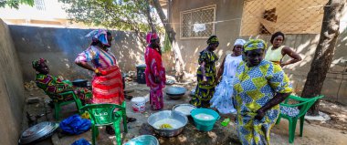 Bour, Senegal - Aralık 2021 civarı. Geleneksel renkte giyinmiş, tanımlanamayan kadınlar açık mutfakta temel gıdalarla yemek pişiriyorlar ama harika yemekler yapıyorlar. Afrika 'da yoksulluk