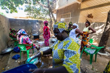 Bour, Senegal - Aralık 2021 civarı. Geleneksel renkte giyinmiş, tanımlanamayan kadınlar açık mutfakta temel gıdalarla yemek pişiriyorlar ama harika yemekler yapıyorlar. Afrika 'da yoksulluk