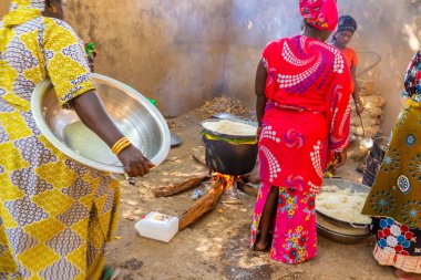 Bour, Senegal - Aralık 2021 civarı. Geleneksel renkte giyinmiş, tanımlanamayan kadınlar açık mutfakta temel gıdalarla yemek pişiriyorlar ama harika yemekler yapıyorlar. Afrika 'da yoksulluk