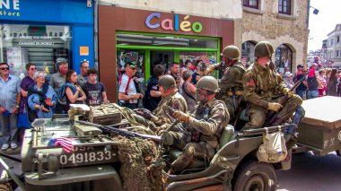 Aziz Michael L 'Eglise, FRANSA - 6 Haziran 2019. Normandiya Çıkarması 'nın kutlanması, silahlı çıkarma, İkinci Dünya Savaşı' nın Normandiya 'da sona ermesi, müttefik ülkelerin yardımıyla. Askerler sokakta izleyicilerle birlikte cipte yürüyorlar.