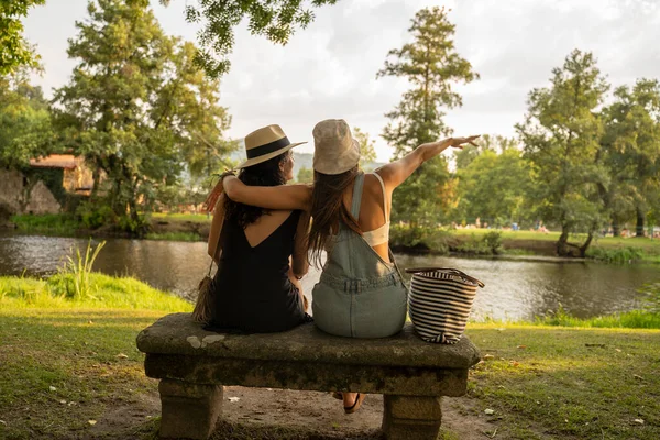 Şapkalı iki arkadaş nehrin önündeki taş bir bankta oturmuş sohbet ediyorlar. Yüksek kalite fotoğraf