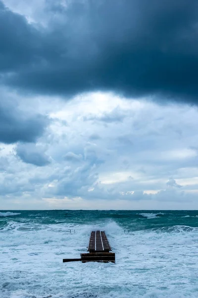 Rough sea waves on pier pointing to horizon with blue thunder clouds