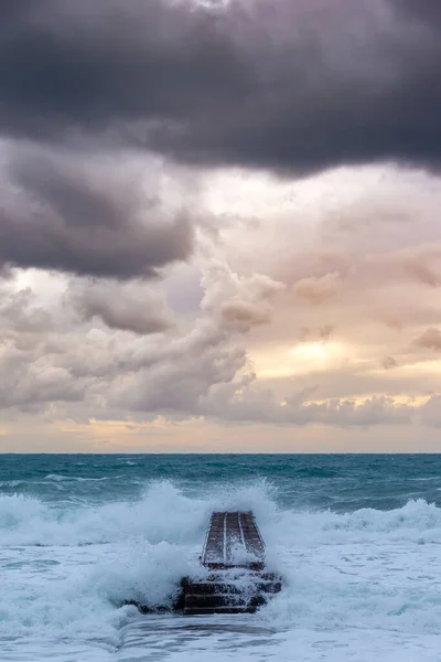 rough crashing waves on a pier with dark and golden clouds after a storm