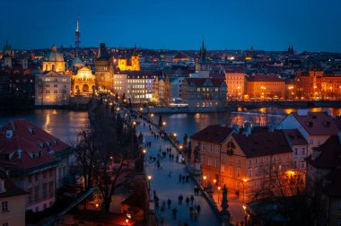 İnsanlar geceleri Charles Köprüsü 'nü harika aydınlatılmış ortaçağ binalarıyla geçiyorlar.