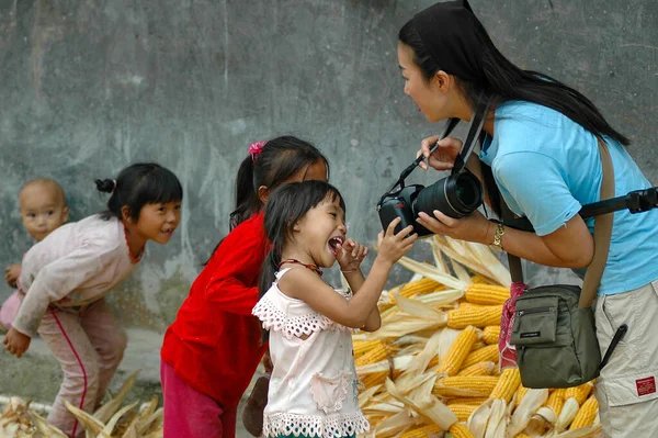 Woman photographer sharing photos on her DSLR camera with excited and happy Miao village children