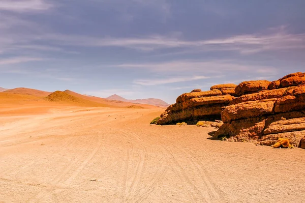 Atacama desert in Chile with tire tracks leading to horizon and interesting orange rock formations