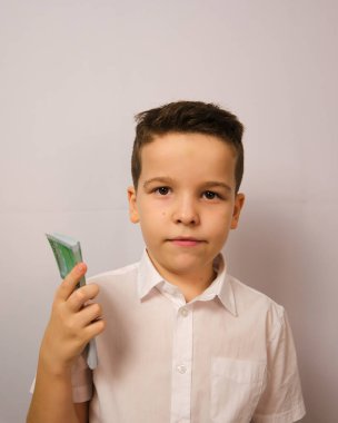 Çocuk kameraya para gösteriyor, kameraya bakıyor beyaz arka planda bir çocuğun fotoğrafını çekiyor, bir çocuk elinde parayla yüzünde duygular gösteriyor.