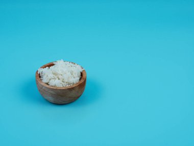 Mavi arka planda izole edilmiş küçük bir ahşap kasede pirinç.