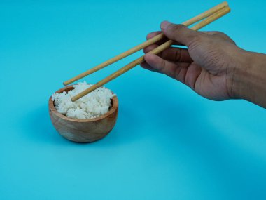 Küçük ahşap kasede yemek çubuklarıyla pirinç alan eller..