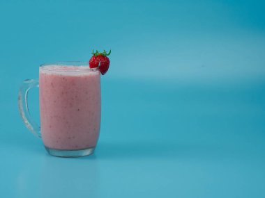 Strawberry milkshake juice in a glass on blue background. healthy fruit drink concept.