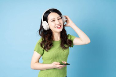 Asyalı çekirge kız portresi müzik dinliyor, mavi arka planda izole edilmiş.