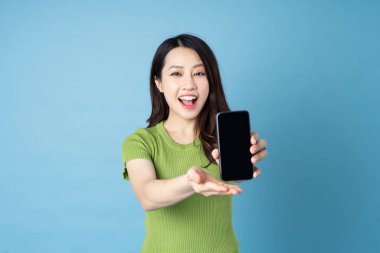 Genç Asyalı bir kızın portresi, elinde telefon, mavi arka planda izole edilmiş.