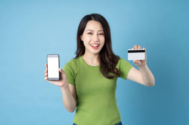 Genç Asyalı bir kızın portresi, elinde telefon, mavi arka planda izole edilmiş.