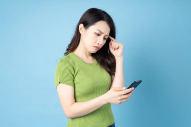 Genç Asyalı bir kızın portresi, elinde telefon, mavi arka planda izole edilmiş.
