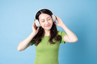 Asyalı çekirge kız portresi müzik dinliyor, mavi arka planda izole edilmiş.