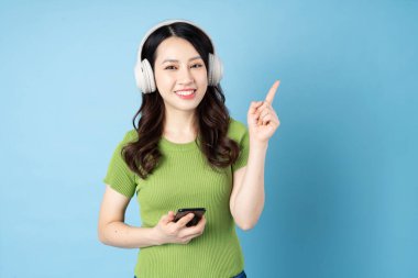 Asyalı çekirge kız portresi müzik dinliyor, mavi arka planda izole edilmiş.