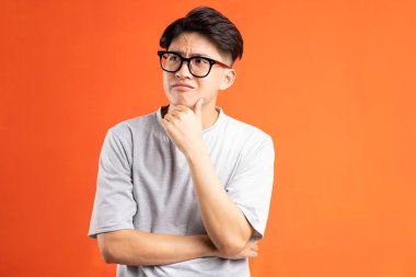 Turuncu arka planda soyutlanmış Asyalı genç adamın portresi.