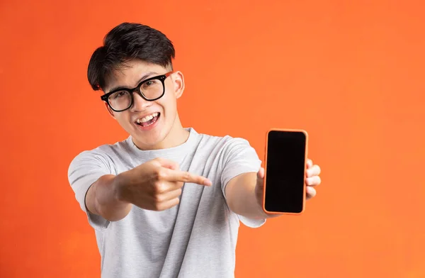 Portrait of young asian man pointing at phone screen, isolated on orange background