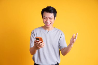 Asyalı genç adam sarı arka planda poz veriyor.