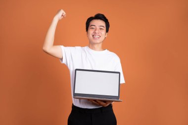 Asyalı adam dizüstü bilgisayar tutuyor, turuncu arka planda izole edilmiş.