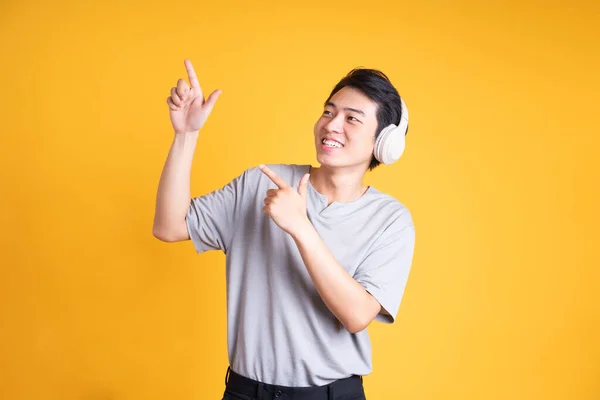 黄色の背景に隔離されたヘッドフォンで音楽を聴くアジア系男性のイメージ — ストック写真