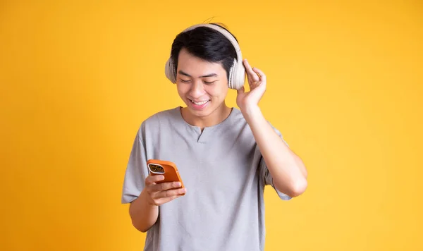 黄色の背景に隔離されたヘッドフォンで音楽を聴くアジア系男性のイメージ — ストック写真