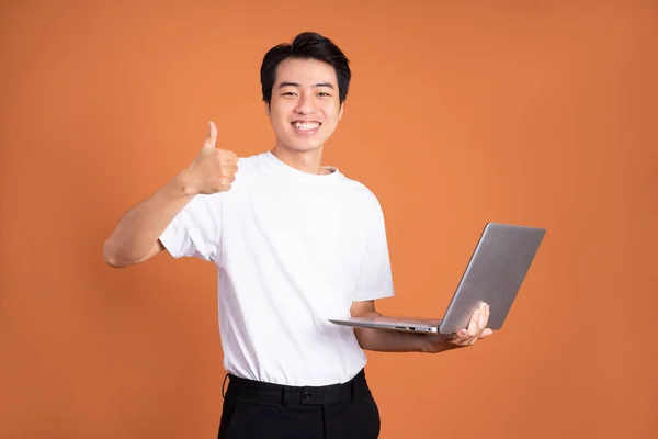 Pria Asia Yang Memegang Laptop Terisolasi Dengan Latar Belakang Oranye — Stok Foto