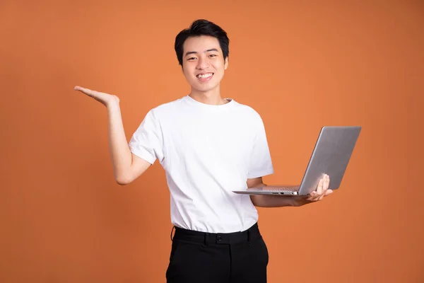 ノートパソコンを持ってオレンジの背景に隔離されたアジア人男性 — ストック写真