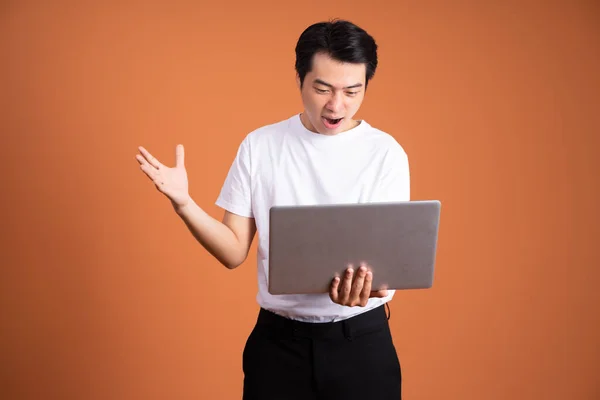 asian man holding laptop, isolated on orange background