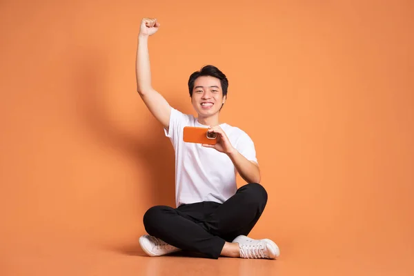 Immagine Uomo Asiatico Seduto Utilizzando Telefono Isolato Sfondo Arancione — Foto Stock