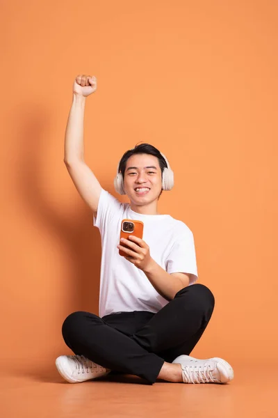 電話で座ってオレンジの背景に隔離されたアジア系男性のイメージです — ストック写真