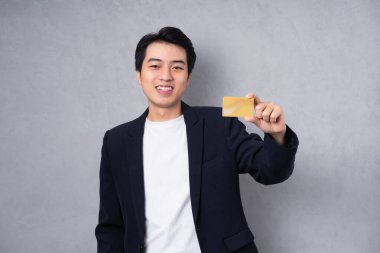 Gri arka planda duran takım elbiseli genç bir iş adamı.