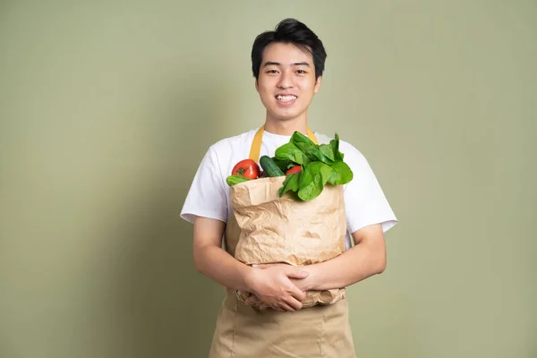 Young man is holding a bag full of vegetables, on white background.