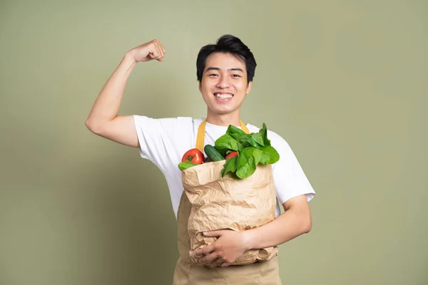 Young man is holding a bag full of vegetables, on white background.