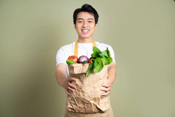 Young man is holding a bag full of vegetables, on white background.