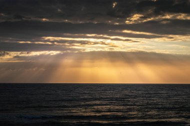 İspanya plajı gün doğumunda kumsalda büyük kayalarla.