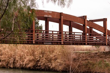 Nehrin üzerinden geçen bitki örtüsüyle çevrili tahta köprü.