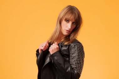 Çekici sarışın bir kadının portresi sarı bir arka planda çivili deri ceket giyiyor.