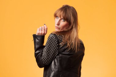 Çekici sarışın bir kadının portresi sarı bir arka planda çivili deri ceket giyiyor.