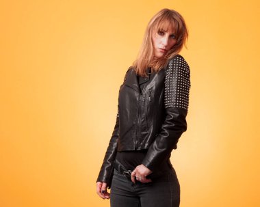 Çekici sarışın bir kadının portresi sarı bir arka planda çivili deri ceket giyiyor.