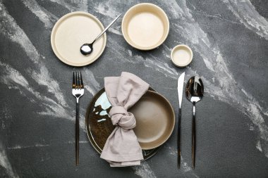 Gri zemin üzerinde çatal bıçak takımı ve bardak olan bir sürü boş tabak.