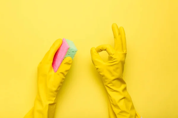 hands in gloves hold a sponge on a yellow background