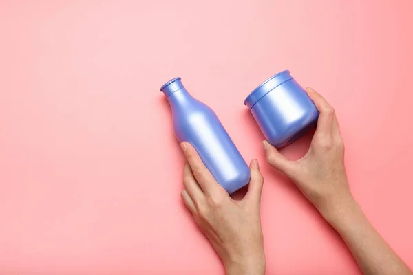 bottle of shampoo in hands on a pink background. Minimalism, place for text. Top view