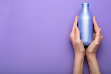 Mor bir arka planda ellerinde bir şişe şampuan. Minimalizm. Üst görünüm