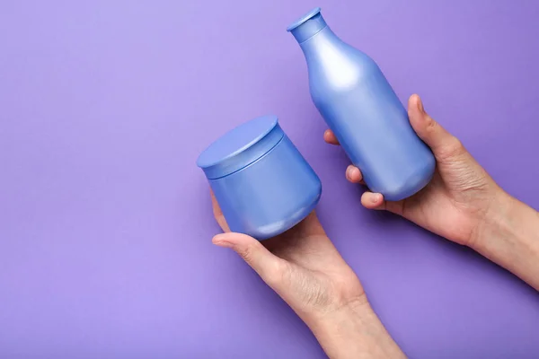 shampoo and hair mask in hands on a purple background. Minimalism, space for text. Top view