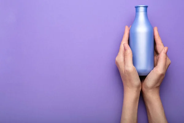 bottle of shampoo in hands on a purple background. Minimalism. Top view
