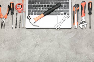 Gri arka planda dizüstü bilgisayarın yanında çeşitli inşaat aletleri var. Ev onarımı için aletler. İnşaat alanında çalışıyorum. Üst Manzara. Metin için boşluk